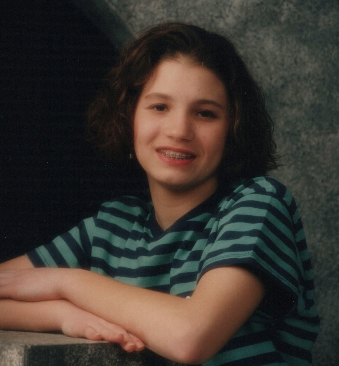 1990s Woman Short Curly Brown Hair Braces Smiling Leaning Marble Surface