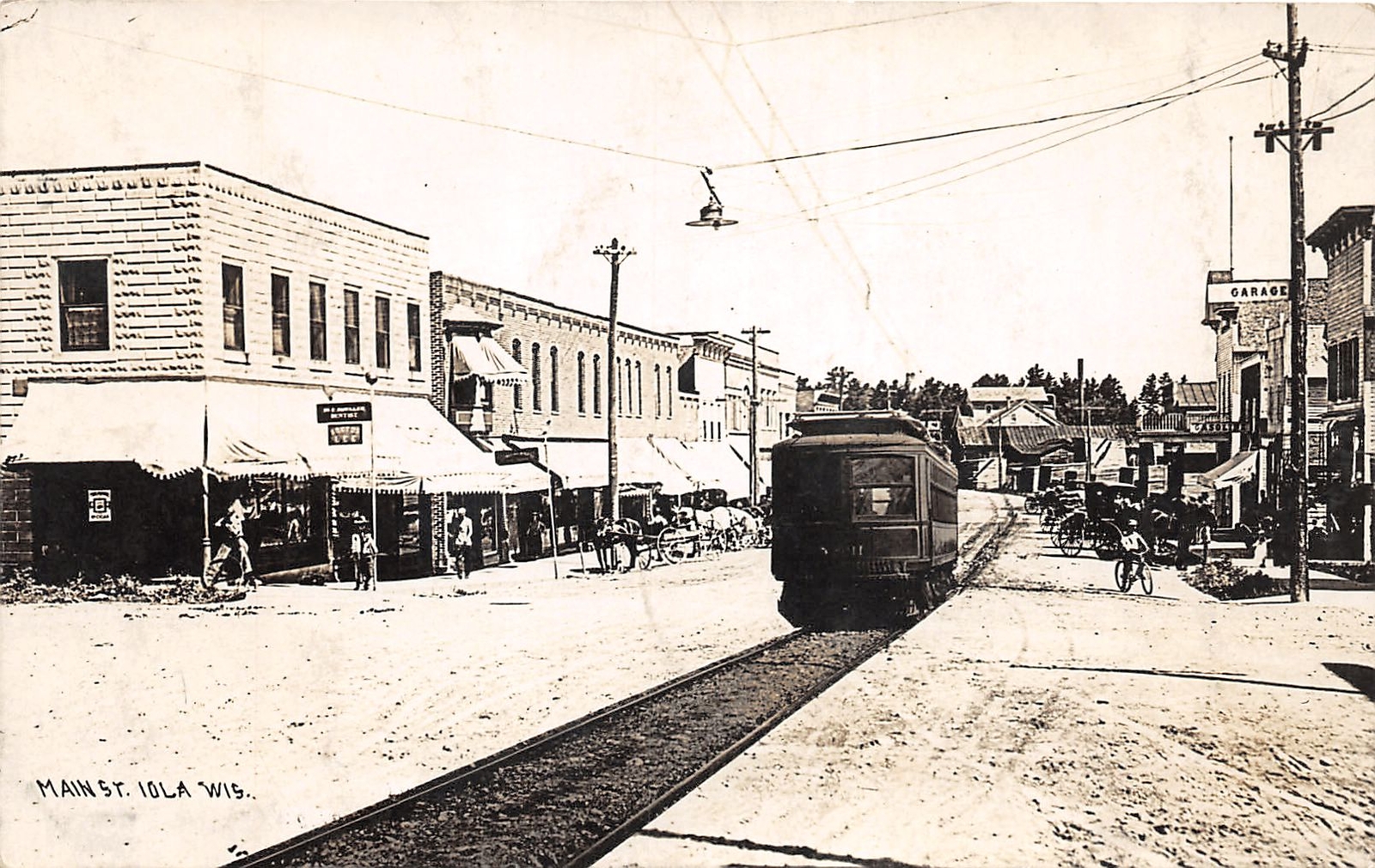J47/ Iola Wisconsin RPPC Postcard c1910 Trolley Stores Main Street 259